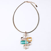 Adjustable Necklace with a brown steel cable chain and a pendant with 6 interlocking squares plated in rose gold and painted in beige, gold, and teal enamel against a white background. Five squares contain square cut outs.