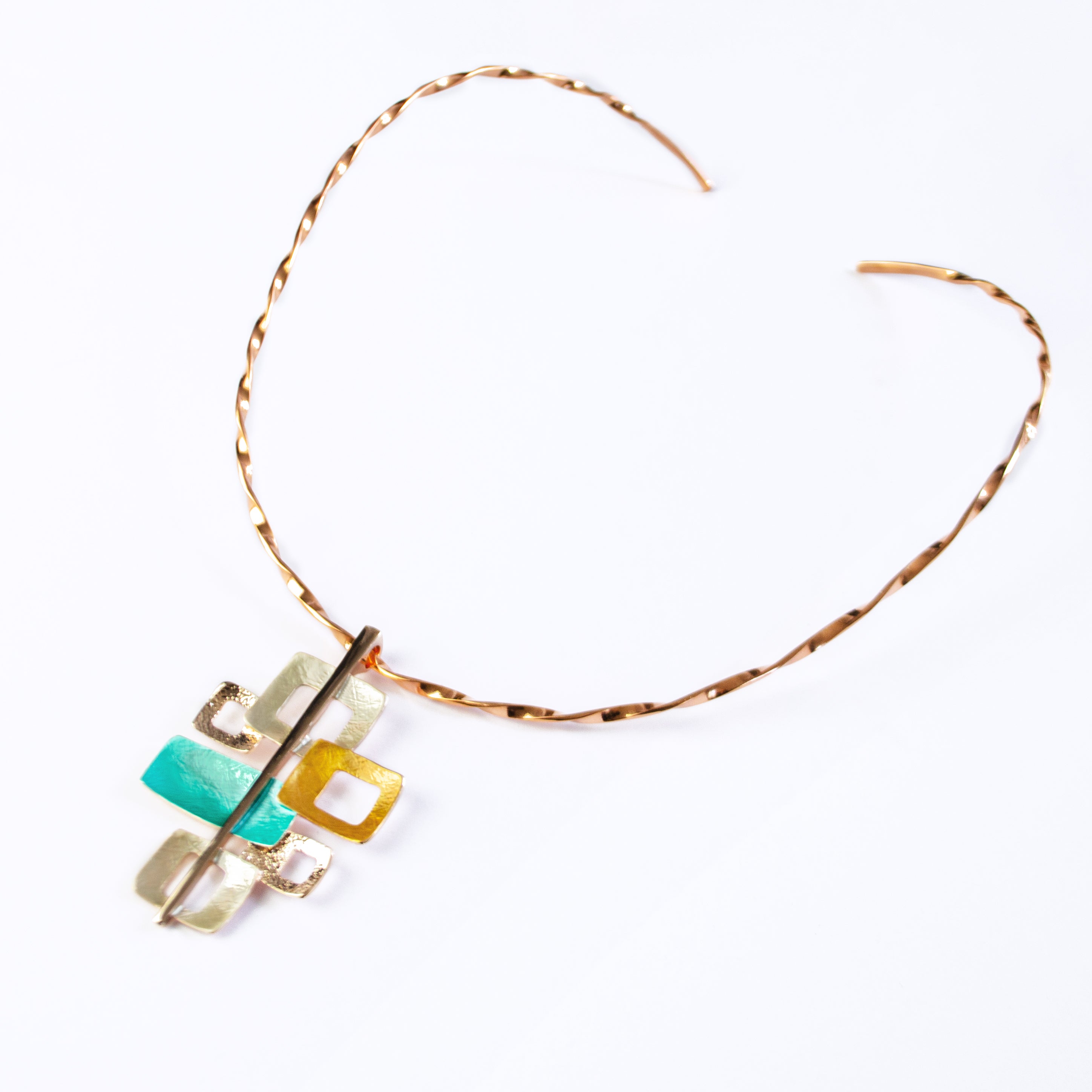 Necklace with a Copper Flat Twist-Wire Neck Ring and a pendant with 6 interlocking squares plated in rose gold and painted in beige, gold, and teal enamel against a white background. Five squares contain square cut outs.