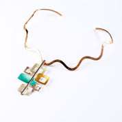 Necklace with a Copper  Wavy Neck Ring and a pendant with 6 interlocking squares plated in rose gold and painted in beige, gold, and teal enamel against a white background. Five squares contain square cut outs.