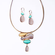 Matching Earring and Necklace Set. Earrings are dangle earrings with two oval shapes painted in teal and brown. Necklace is a pendant with three organic shapes and a dangling teardrop painted in gold, brown, and teal. Necklace has a Steel wire chain