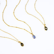 Oval natural tanzanite Cabochon, Black Star Sapphire and Black Copper Obsidian Bezel Set into a 925 Sterling Silver Pendant Plated in 18k Vermeil Gold sitting on a 14K Gold Filled Cable Chain resting on a white background. Great as a gift for fall lovers and blue color and sunstone lovers.