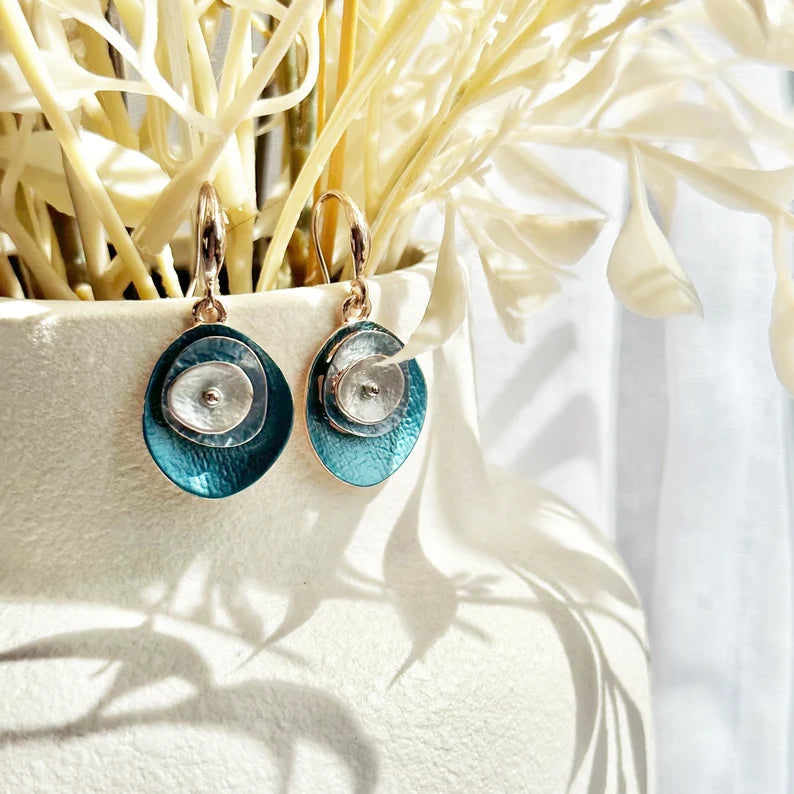 A pair of blue boho abstract flower earrings hand on the edge of a white vase with cream colored flowers. These earrings can be created in any color combination you like, making these the perfect gift to complete anyone's jewelry collection. These easy-breezy bohemian style layered disc dangle earrings are comfortable to wear and add a subtle pop of color. Wear them on their own, or go big and pair them with their matching abstract flower necklace. 