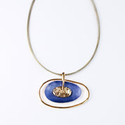 rose gold plated Open Oval Pendant with two textured overlapping oval disks in the center, painted in blue enamel and sitting on a brown steel wire chain against a white background