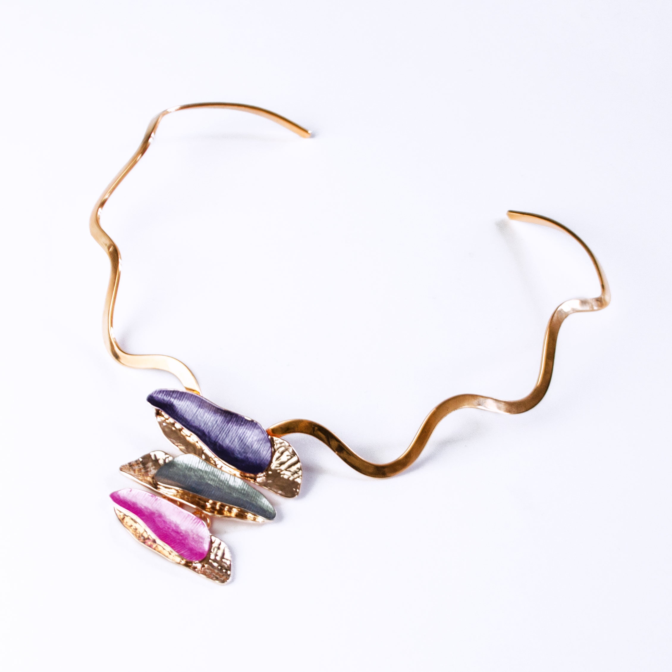 Necklace with a copper wavy neck ring and a rose gold plated pendant made of three sets of two overlapping long organic bar shapes with the top painted in enamel of either purple, gray, or pink. Necklace sits against a white background.