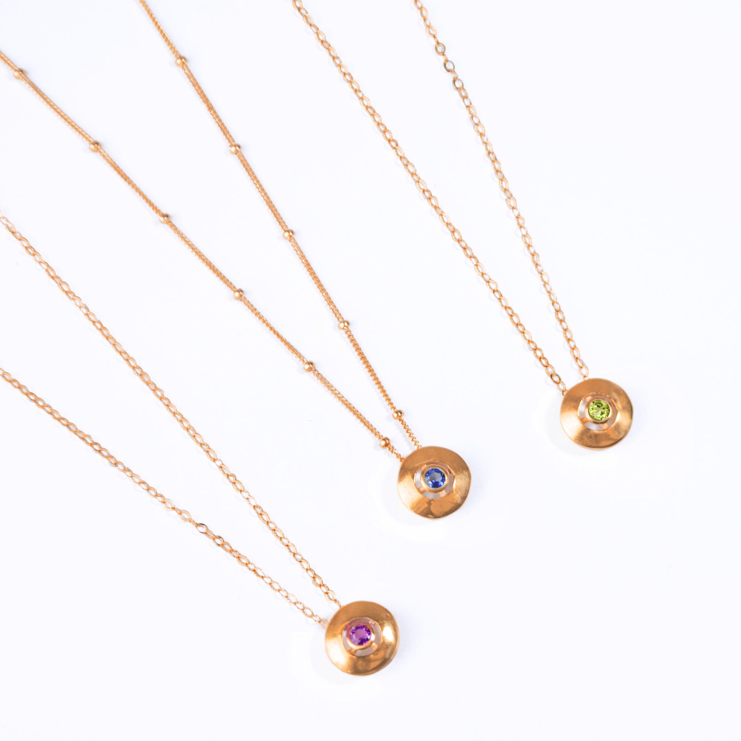 Three Necklaces with Bezel Set Round Pendants. Pendants are 18k Vermeil Rose Gold with 14k Rose Gold Filled Chains. From Left to Right: Purple Amethyst Pendant on a cable chain, Kyanite Pendant on a Satellite Chain, Peridot Pendant on a cable chain