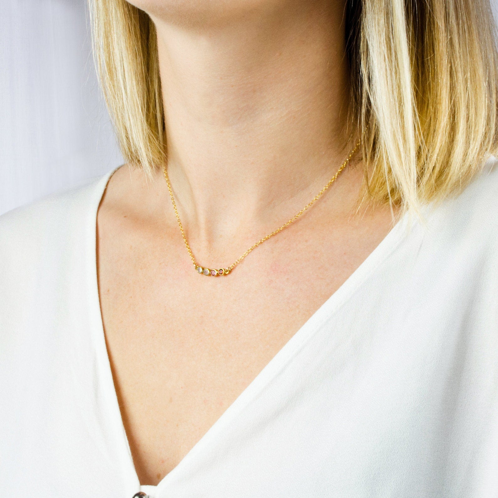 Model in white top is wearing a four stone dainty birthstone necklace featuring garnet, ruby, pink chalcedony and aqua chalcedony. 