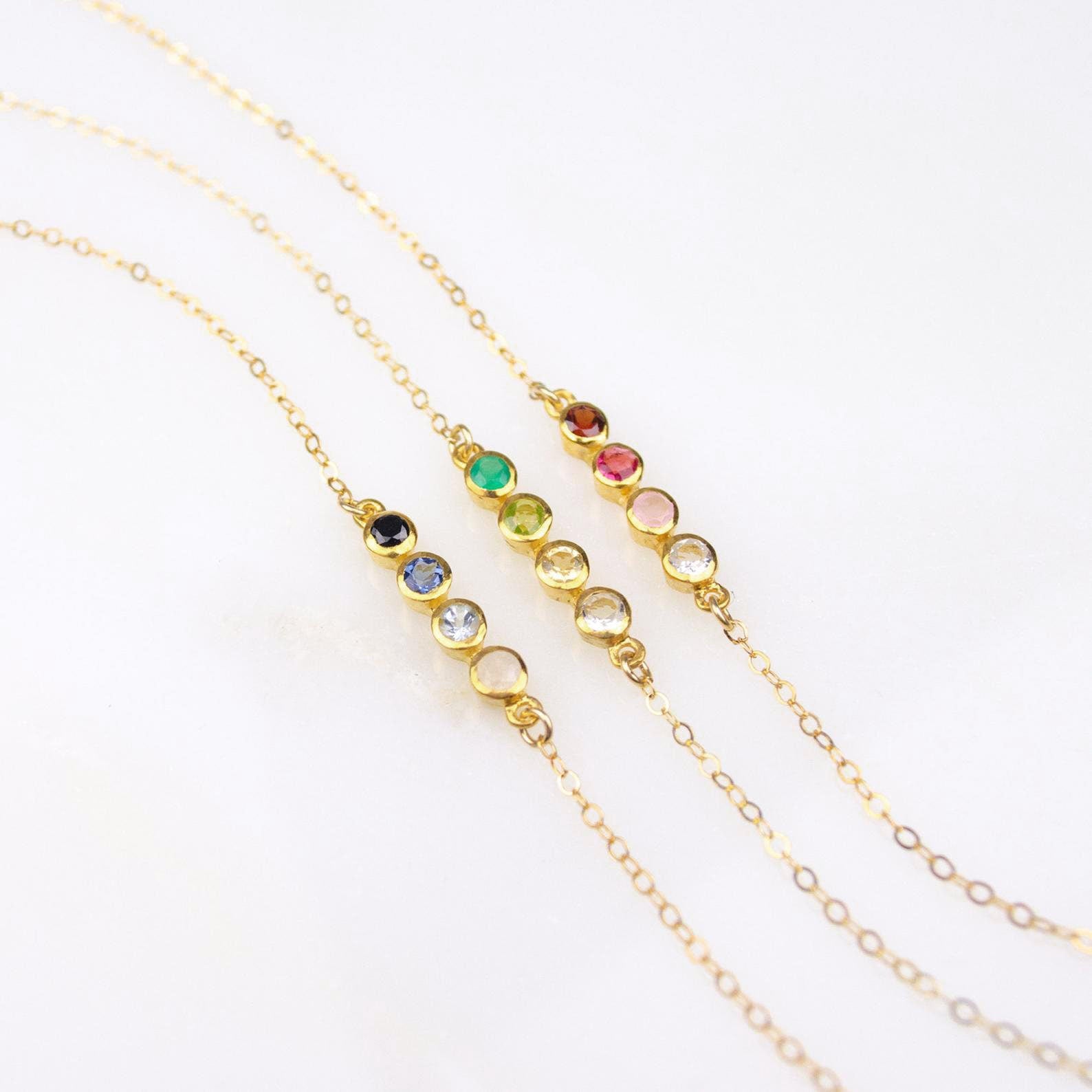 Three necklaces each with a four stone bar dainty birthstone necklace featuring garnet, ruby, pink chalcedony and aqua chalcedony. One featuring green onyx, peridot, citrine and clear. One featuring black onyx, kyanite, blue topaz and moonstone