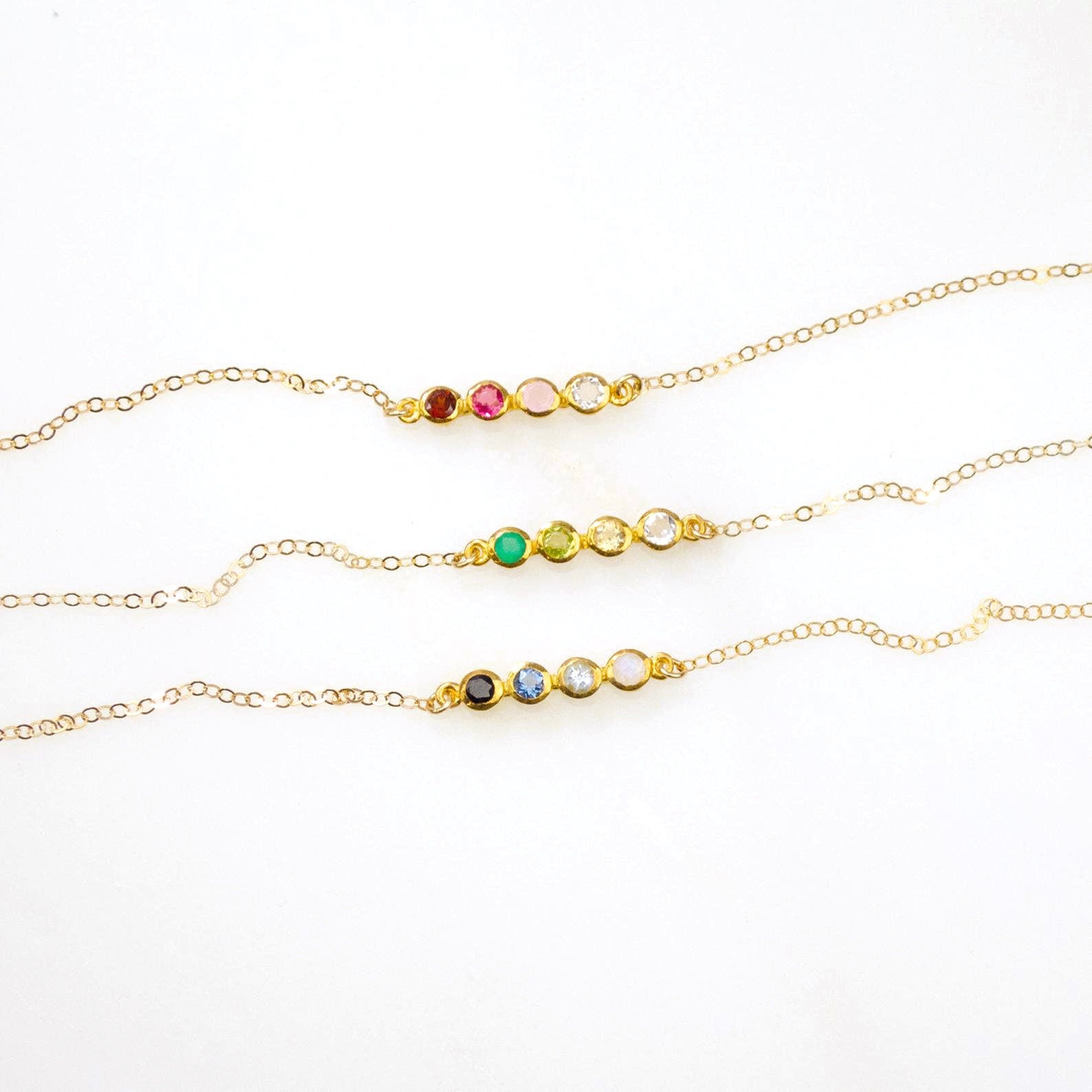 Three necklaces each with a four stone bar dainty birthstone necklace featuring garnet, ruby, pink chalcedony and aqua chalcedony. One featuring green onyx, peridot, citrine and clear. One featuring black onyx, kyanite, blue topaz and moonstone on white background