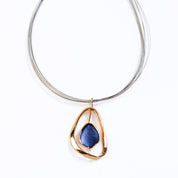 Adjustable Necklace with a brown steel wire chain and an open Pear shape rose gold pendant with a floating textured disc center painted in blue enamel on a white background