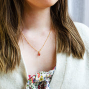 Model wears an oval cabochon ruby quartz prong set on a 925 Sterling Silver pendant plated in 18k Vermeil Gold sitting on an 18 inch 14k gold filled Satellite Chain