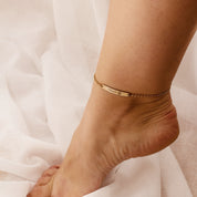 Model is wearing a single 5x30 paw print bar anklet in gold filled with an engraved name