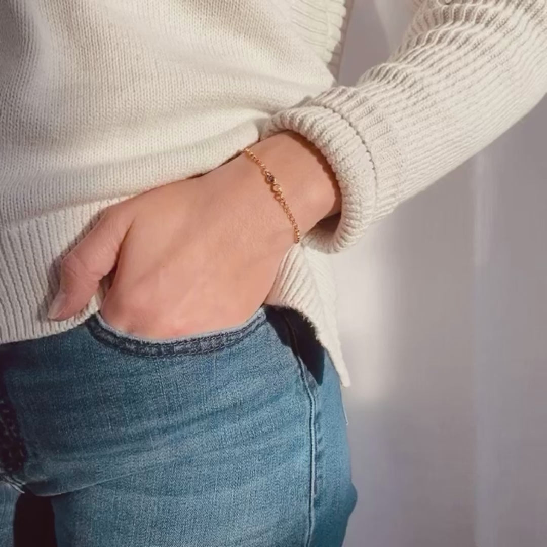 A person in a white long sleeve sweater wears a dainty minimalist birthstone bar bracelet with their hand tucked into their pocket. The words Meaningful & Minimalist sit next to 4 bar bracelets sliding into frame one at a time. A close up of a person's wrist shows a gold, silver and rose gold bracelet with different numbers of stones. A person shows a close up of a 4 stone gold bar bracelet with quartz, pink chalcedony, ruby and garnet. A person in a white shirt opens a red Jewelry box revealing a bracelet.