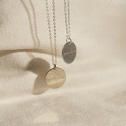 2 disc necklaces engraved with the words "soulmate" and "grandma" sway and reflect light against a tan background. These personalized dainty necklaces are perfect gifts for grandma, mom, your best friend, or anyone who would love something sentimental and unique. Customize each side with your custom engraving, etched into the metal to withstand the test of time. Each piece is good for daily wear and is hypoallergenic, and is easy to clean with a soft microfiber jewelry cloth. Choices are silver, rose/gold.