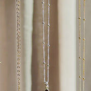 The camera pans down to reveal three vertical bar necklaces in rose gold, silver and gold. A person wears a short necklace with a dainty 2 stone bar pendant in gold. A person holds up a 3-stone pendant to show off the beautifully faceted dainty birthstones. A person shows a silver necklace in an open red Danique Jewelry box. Perfect for Christmas, Mother's Day or birthdays for Mom or Grandma. 