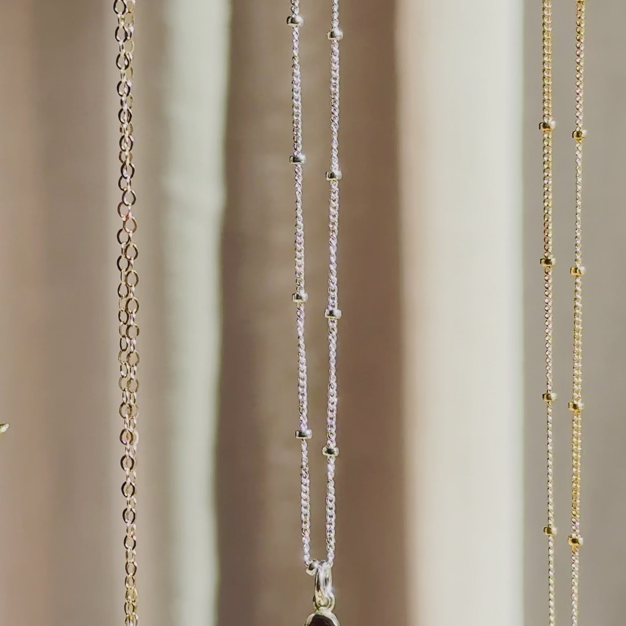 The camera pans down to reveal three vertical bar necklaces in rose gold, silver and gold. A person wears a short necklace with a dainty 2 stone bar pendant in gold. A person holds up a 3-stone pendant to show off the beautifully faceted dainty birthstones. A person shows a silver necklace in an open red Danique Jewelry box. Perfect for Christmas, Mother's Day or birthdays for Mom or Grandma. 