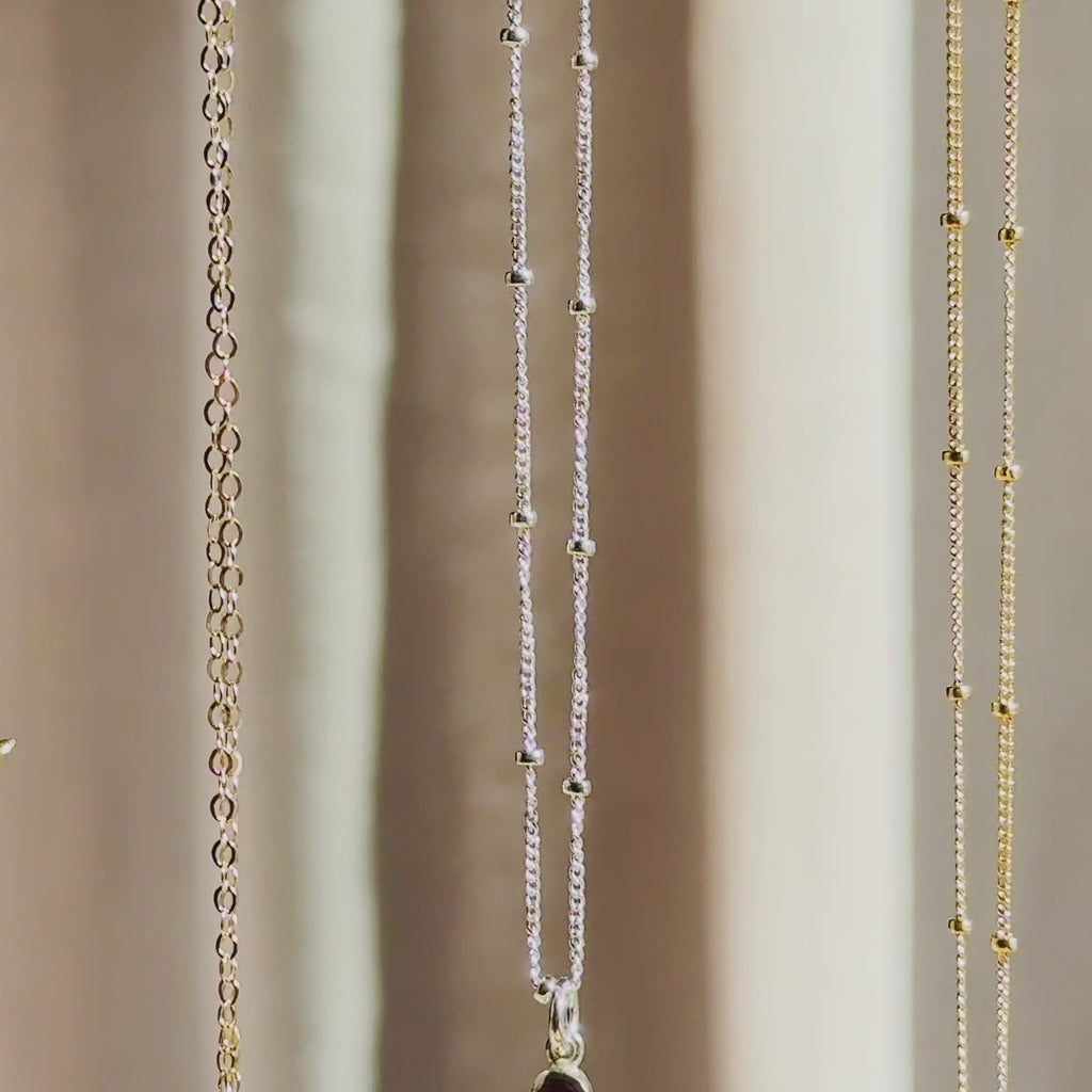 The camera pans down to reveal three vertical bar necklaces in rose gold, silver and gold. A person wears a short necklace with a dainty 2 stone bar pendant in gold. A person holds up a 3-stone pendant to show off the beautifully faceted dainty birthstones. A person shows a silver necklace in an open red Danique Jewelry box. Perfect for Christmas, Mother's Day or birthdays for Mom or Grandma. 