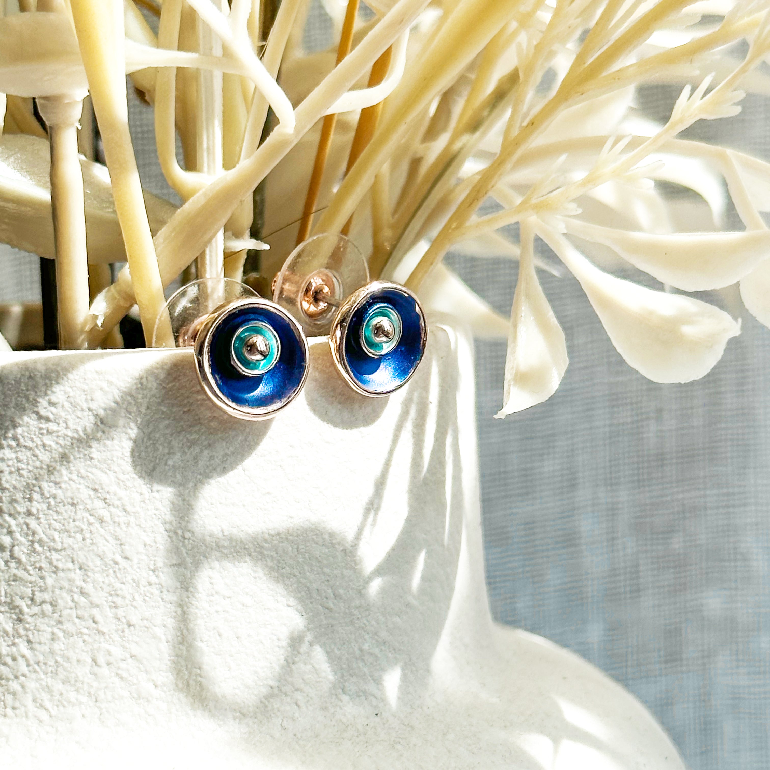 A pair of circular abstract flower earrings against a white background with rose gold plating and painted in blue and teal