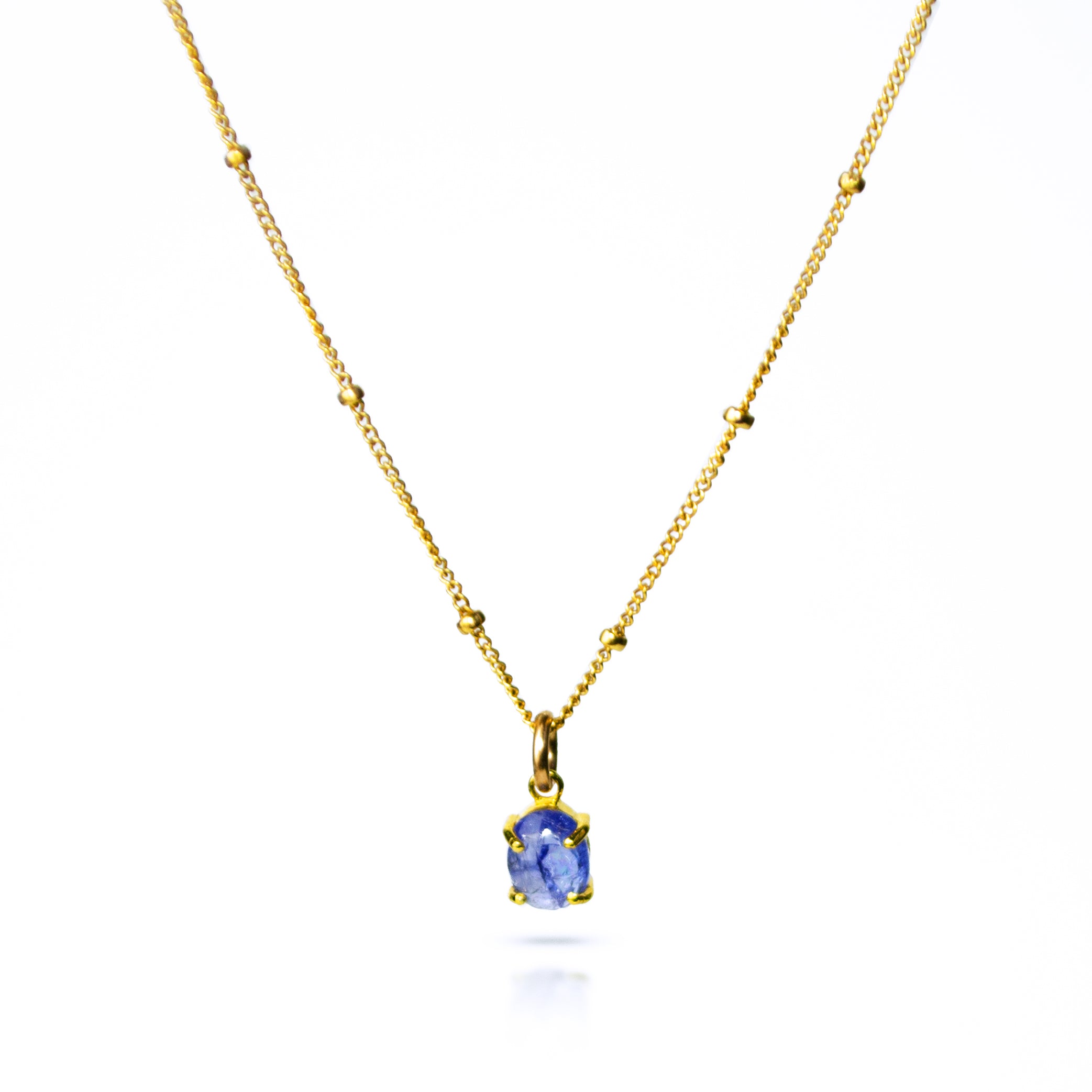 Oval natural tanzanite Cabochon Bezel Set into a 925 Sterling Silver Pendant Plated in 18k Vermeil Gold sitting on a 14K Gold Filled Cable Chain resting on a white background. Great as a gift for fall lovers and sophisticated blue color and sunstone lovers.