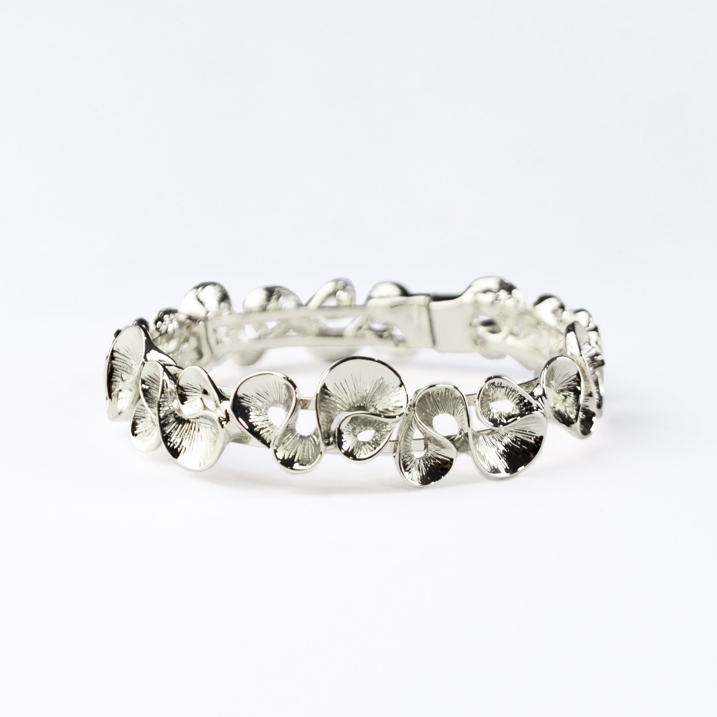 Silver Boho Style Wave Bangle Bracelet with magnetic clasp rests on a dark flat stone with leaves in the background