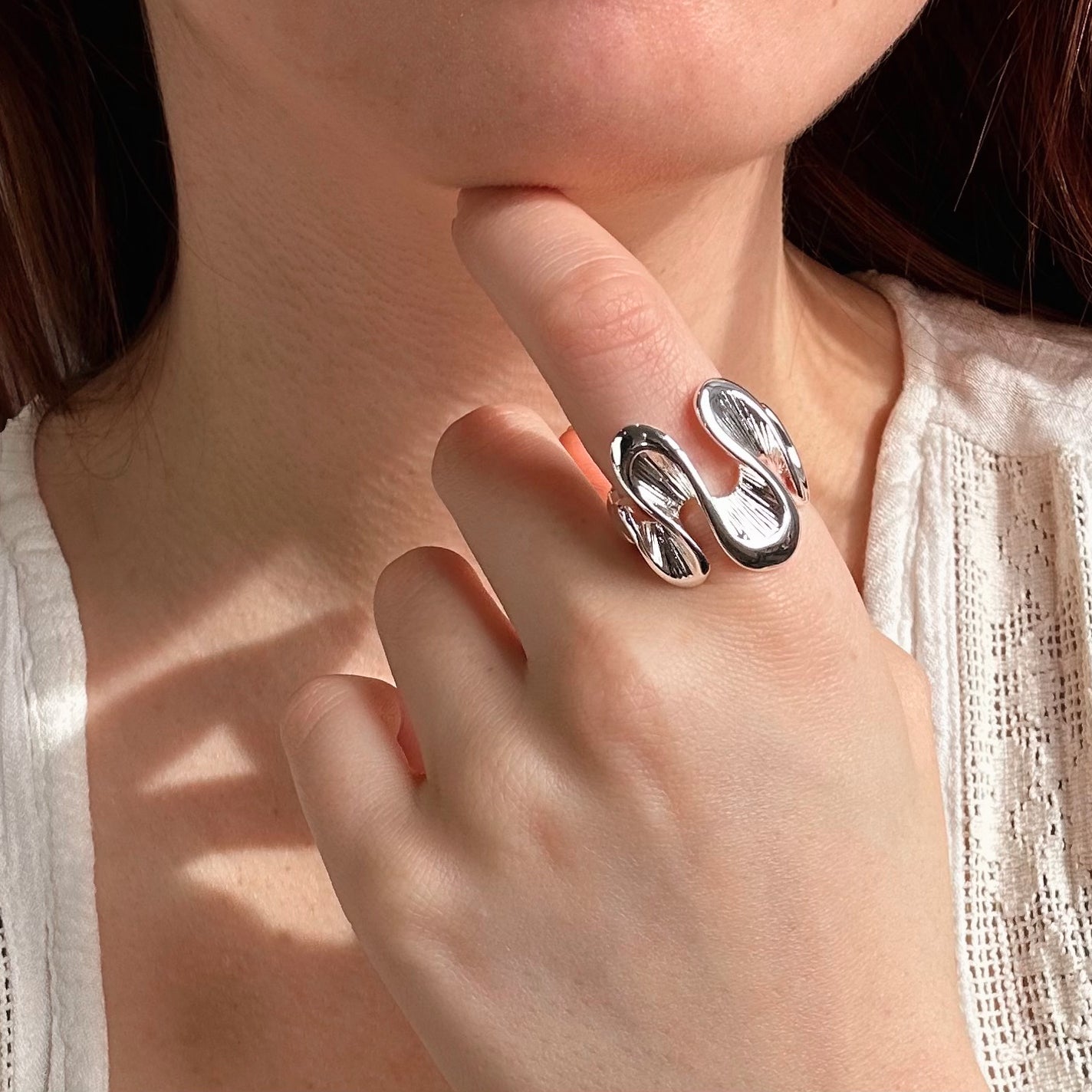 Model wears silver textured wave shaped ring on index finger.