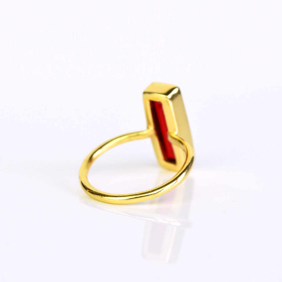 A garnet gemstone bar ring in gold shows an open back setting. 