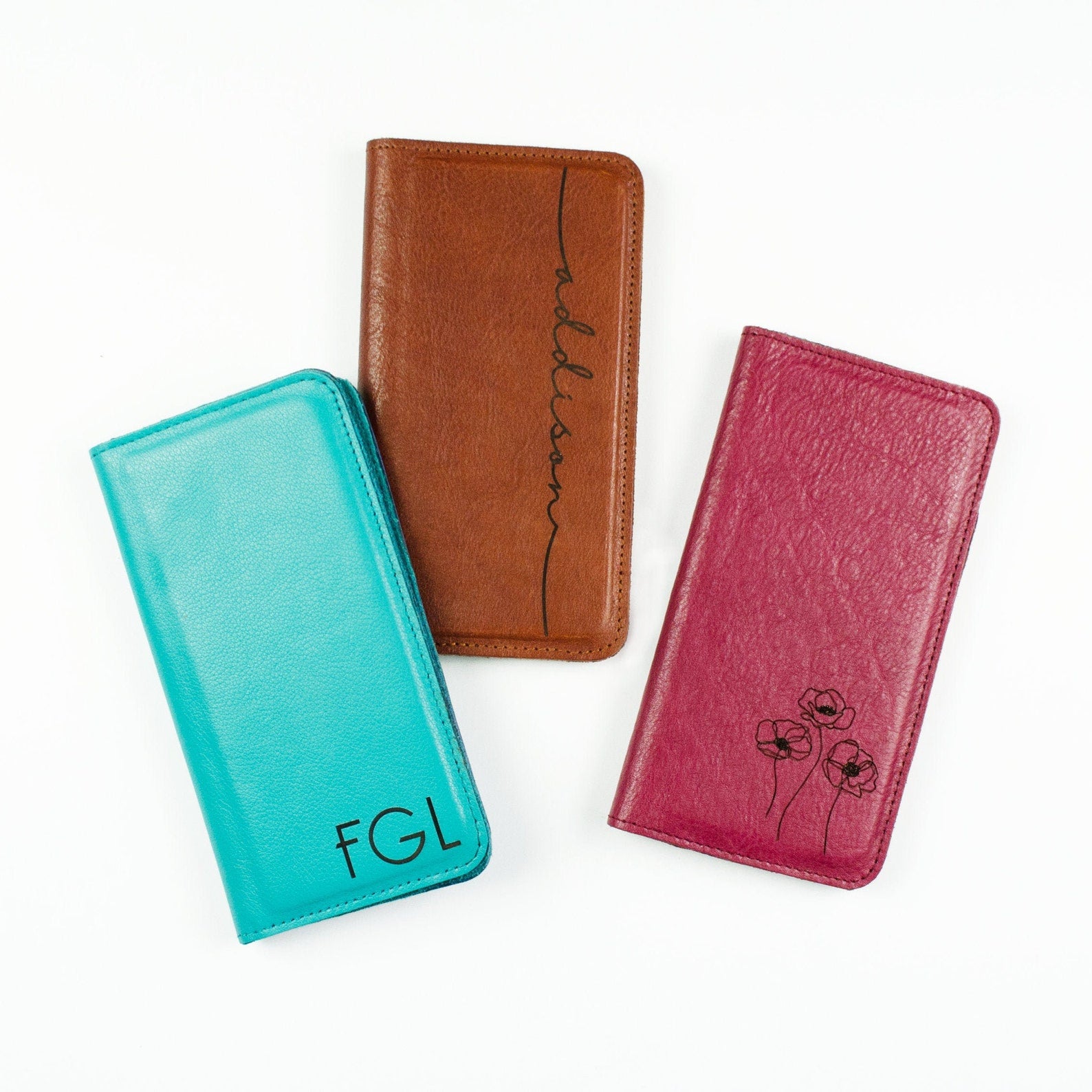 Three genuine leather phone cases, one turquoise case with three initials, honey case with engraved name and raspberry case with flower design on front. 