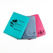 Three Personalized Engraved Leather Passport holders custom engraved for a honeymoon or anniversary gift. Turquoise Passport Holder with the text “Worry Less, Wander More’ and an image of palm trees on a beach engraved on the front, a Lavender Passport Holder with an engraved name and paper plane art, and a Pink Passport Holder with an engraved Monogram. 