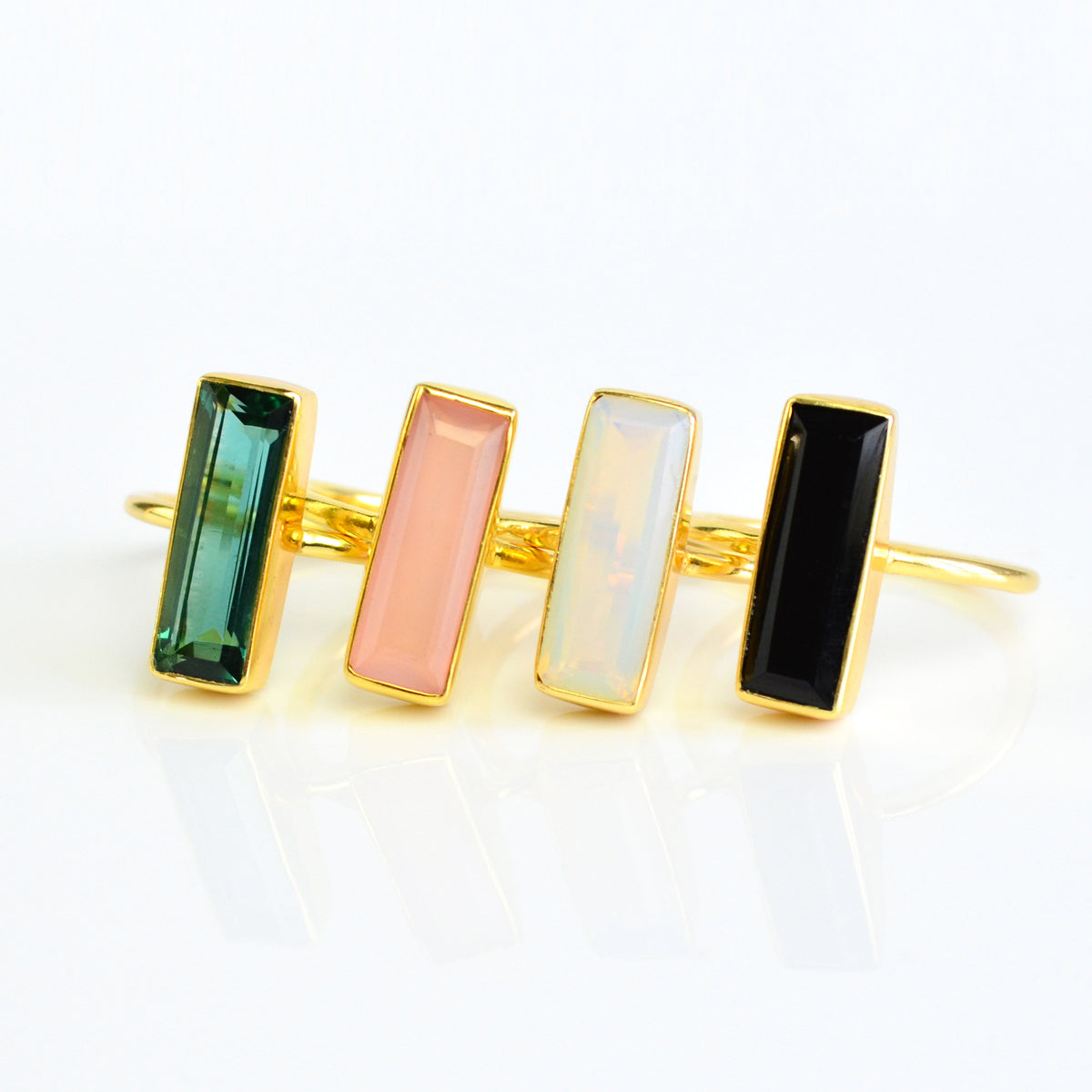 A set of four gemstone bar rings green tourmaline, pink chalcedony, opalite, black onyx, set in gold. Custom gemstone birthstone jewelry. sleek minimalist birthstone rings january, february, march, april, may, june, july, august, september, october, november, december