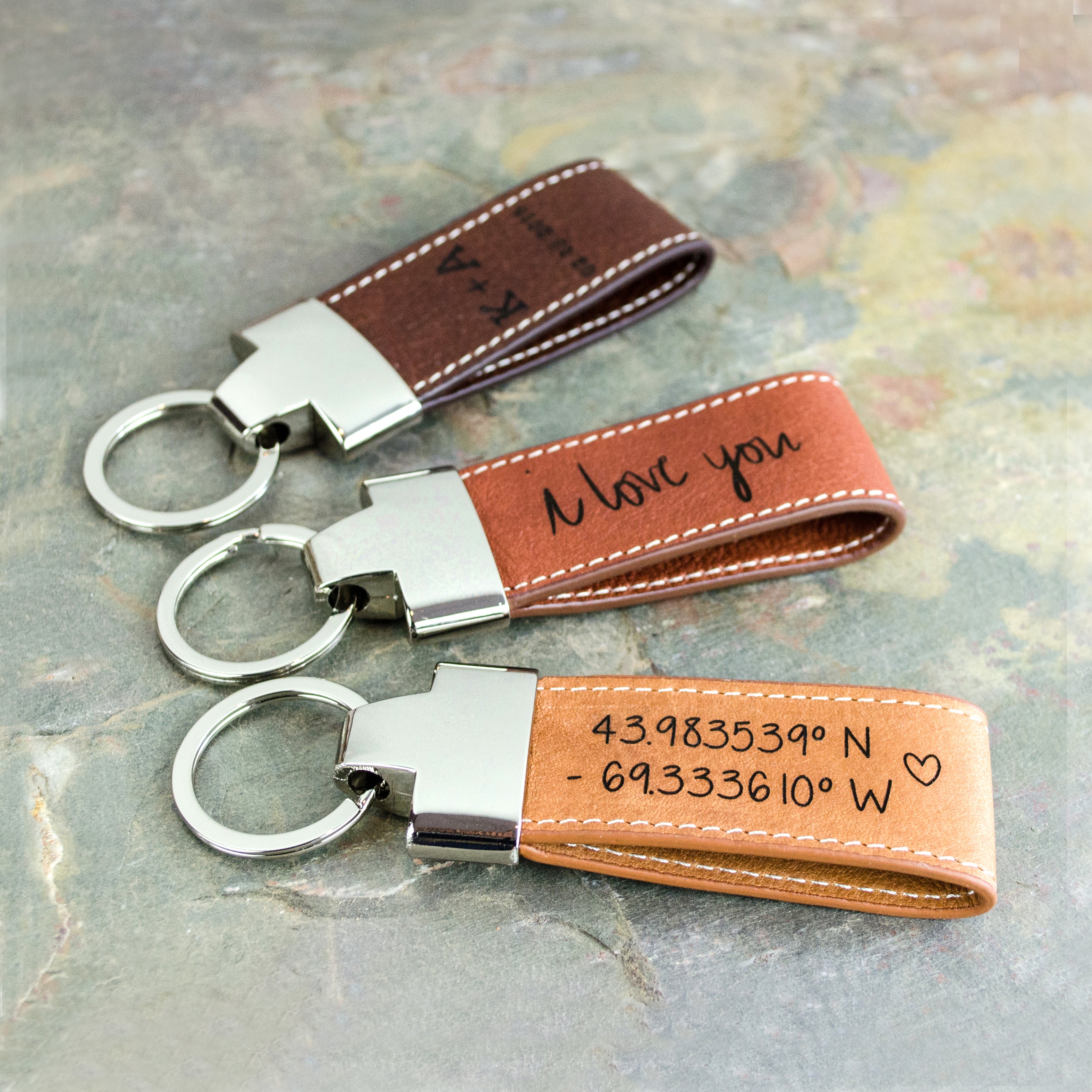 3 leather loop keychains in brown honey, warm cinnamon, and dark espresso are all sitting on a granite background. Coordinates keychains, customized keychain, gift for trucker, gift for new driver, engrave custom handwriting