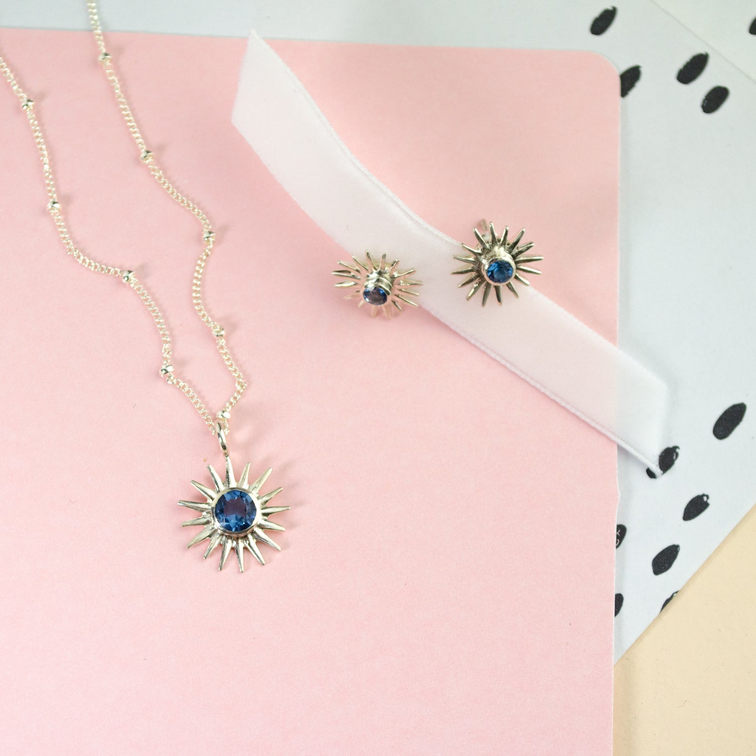 Matching Sun Burst Necklace and Stud Earring Set resting on a pink paper with a white ribbon. 3mm Blue September Birthstone Kyanite bezel set Sterling Silver Sun Stud Earrings with matching 5mm Kyanite Sun Burst Sterling Silver Pendant on a Sterling Silver Cable Chain. September Birthday Gift, Jewelry Set for Her, summer jewelry set, sun jewelry set