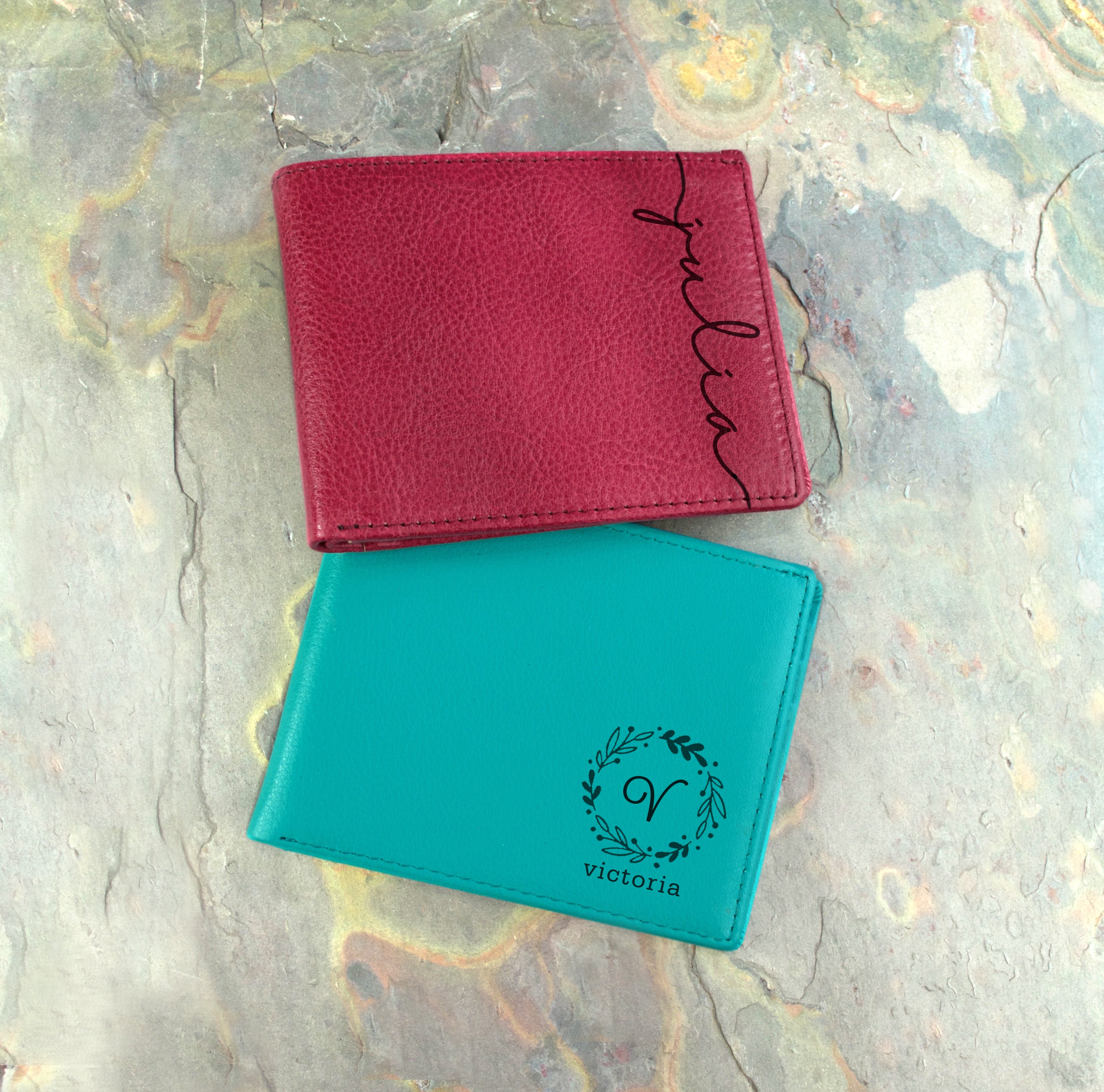 Two personalized wallets one raspberry wallet with name engraved in script font a turquoise wallet with name last initial and wreath part of out monogram collection.